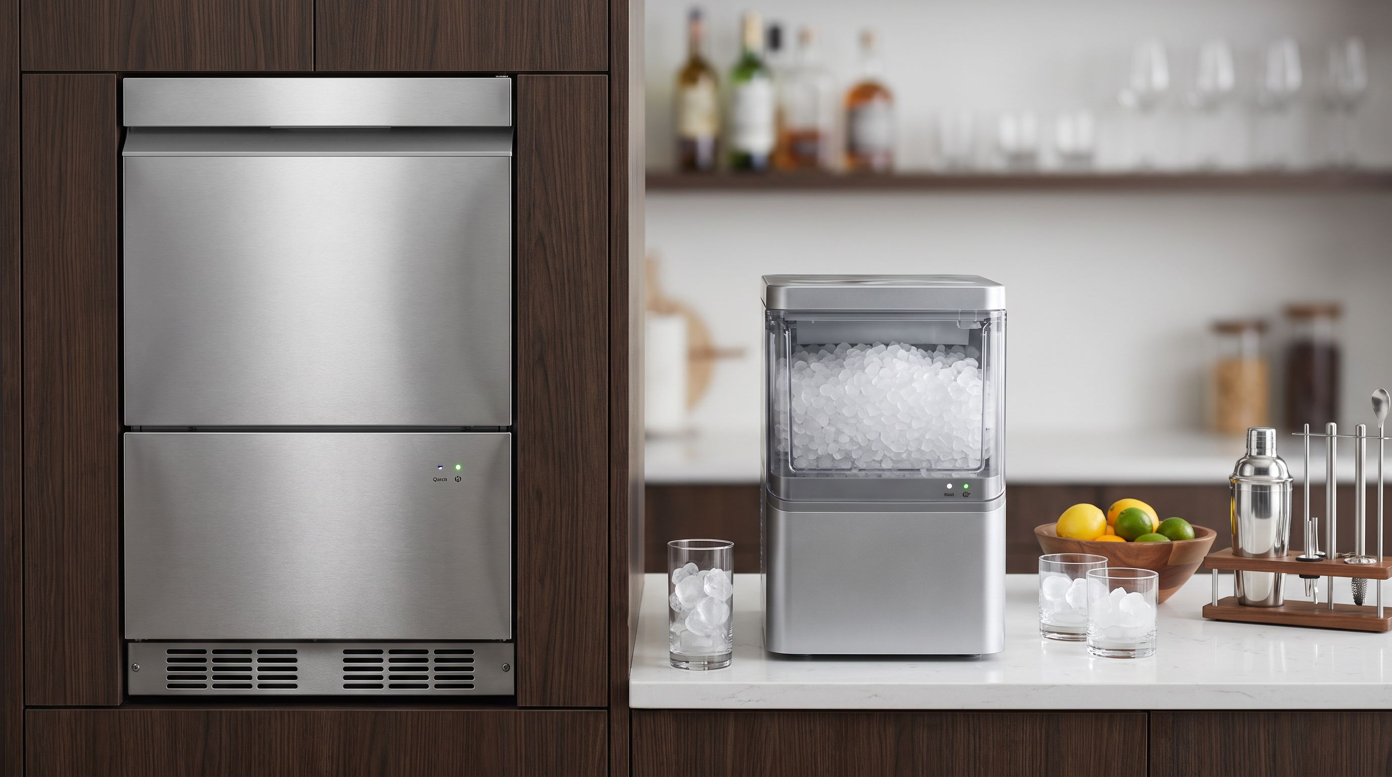 A stainless steel undercounter ice maker built into a home bar cabinet beside a countertop nugget ice maker filled with pebble ice